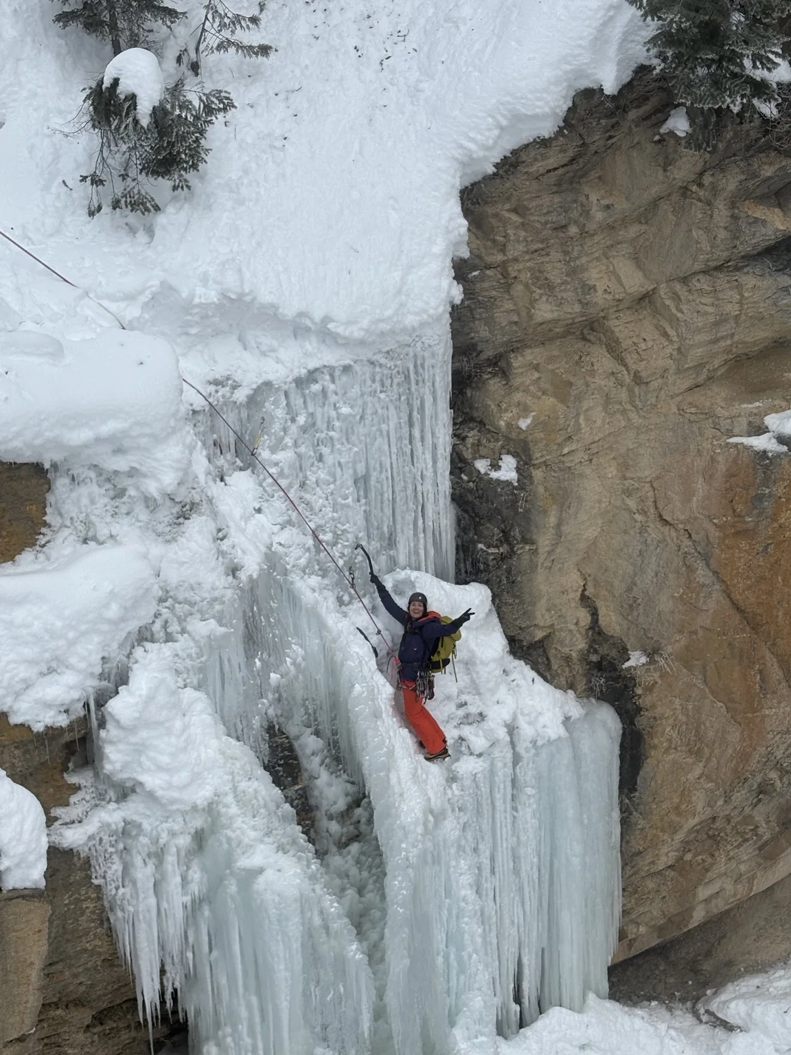 A roped climber in red trousers on a frozen waterfall near camp