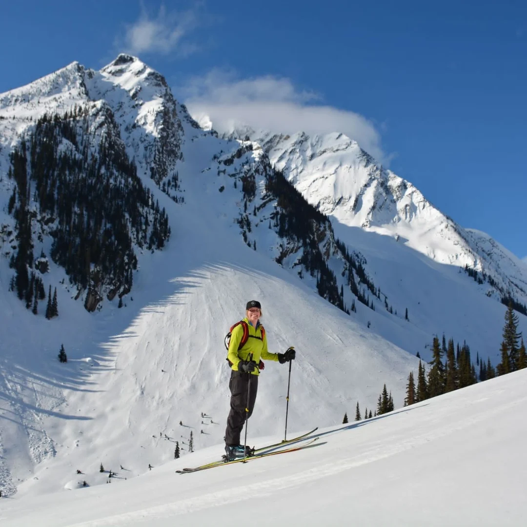 Skier standing below a forested mountain ridge